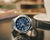 Zegarek męski Casio G-Shock w widoku 3/4 z niebieską tarczą i srebrną metalową bransoletą